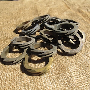 May include: A collection of wooden bracelets in various shades of brown and gold. The bracelets have carved or textured designs, with some appearing to have a spiral pattern. They are arranged on a textured, tan fabric.