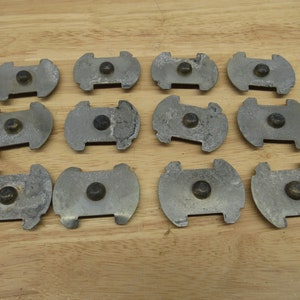 May include: Twelve silver-colored metal discs with a small, round, black button in the center of each disc. The discs are arranged in four rows of three discs each.