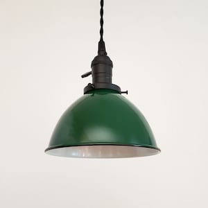 May include: A green pendant light with a black cord and a white interior. The light is hanging from a white ceiling.