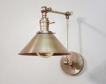 May include: A gold metal wall sconce with a swivel arm and a cone-shaped shade. The sconce has a vintage industrial style.