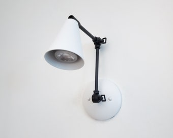 May include: A white wall-mounted lamp with a black adjustable arm and a white cone-shaped shade.