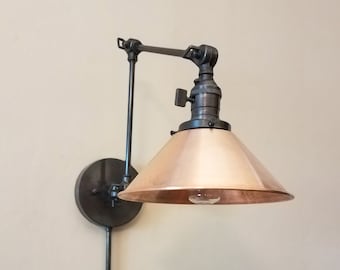 May include: A black metal wall sconce with a copper-colored shade. The sconce has a long arm that extends out from the wall and a smaller arm that holds the shade. The shade is a cone shape and has a light bulb inside.