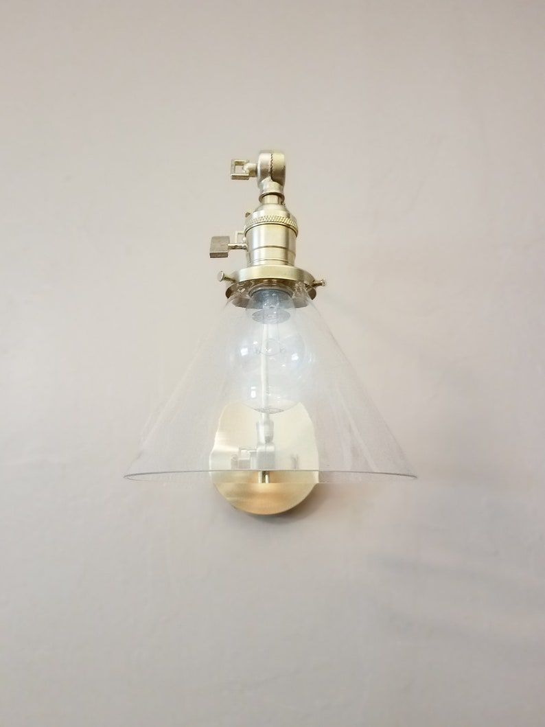 May include: A gold-toned wall sconce with a clear glass cone shade. The sconce has a simple design and is perfect for adding a touch of modern style to any room.