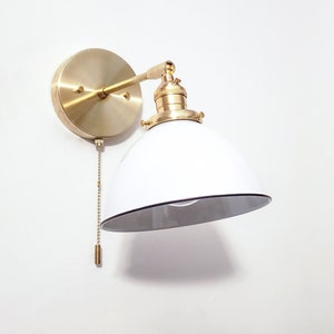 May include: A brass wall sconce with a white enamel shade and a pull chain switch. The shade has a black rim.