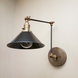 May include: A black and brass wall-mounted light fixture with a black metal shade and a round brass base.
