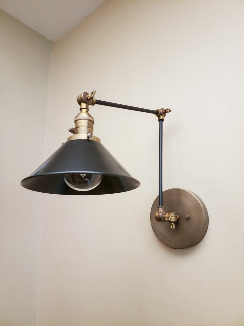 May include: A black and brass wall-mounted light fixture with a black metal shade and a round brass base.