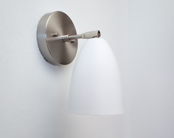 May include: A white wall mounted light fixture with a white shade and a silver base.