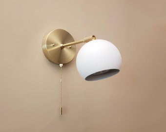 May include: A white globe wall sconce with a brass arm and base. The sconce has a pull chain for turning the light on and off.