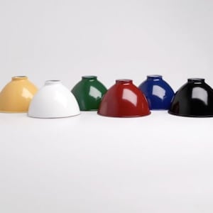 May include: Six metal lampshades in different colors: yellow, white, green, red, blue, and black. The lampshades are all the same size and shape, and they are arranged in a row on a white surface.