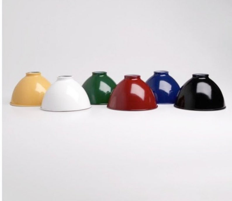 May include: Six metal lampshades in different colors: yellow, white, green, red, blue, and black. The lampshades are all the same size and shape, and they are arranged in a row on a white surface.