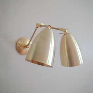 May include: A brass wall sconce with two adjustable,  gold-toned,  bell-shaped shades.