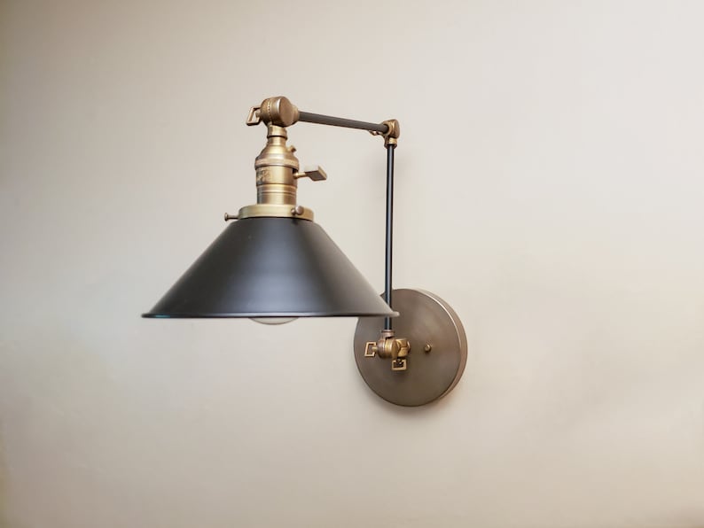 May include: A black and brass wall-mounted light fixture with a black metal shade and a swivel arm. The light fixture has a vintage industrial style.