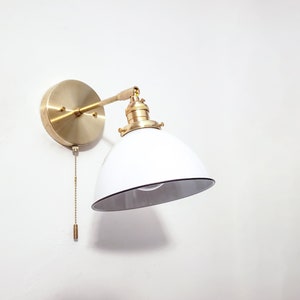 May include: A brass wall sconce with a white, dome-shaped shade and a pull chain switch.