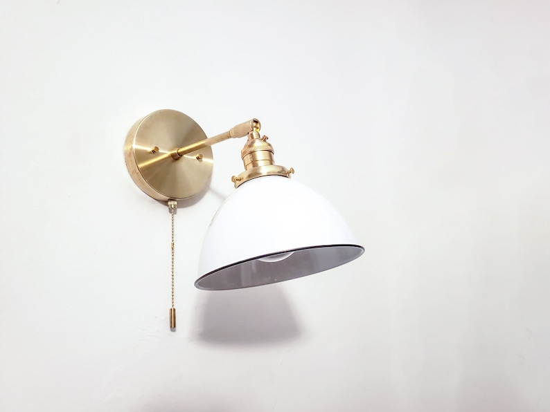 May include: A brass wall sconce with a white, dome-shaped shade and a pull chain switch.
