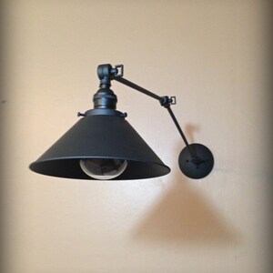 May include: Black wall-mounted light fixture with a black metal shade and a single light bulb. The fixture has a long, adjustable arm.