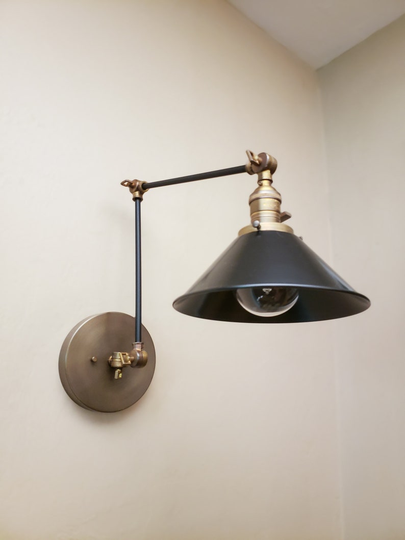 May include: A black and brass wall-mounted light fixture with a black cone-shaped shade and a round brass base.