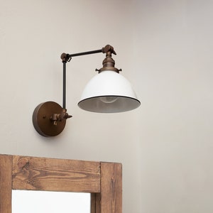 May include: A white and black industrial style wall sconce with a swivel arm. The sconce has a white enamel shade and a brass finish.