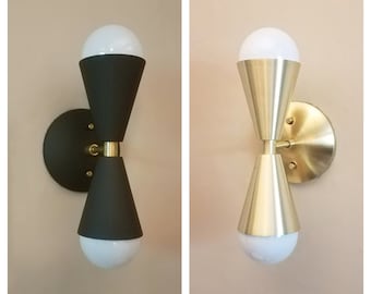May include: Two wall sconces with a modern design. The sconces have a cone shape and are available in black and gold finishes.