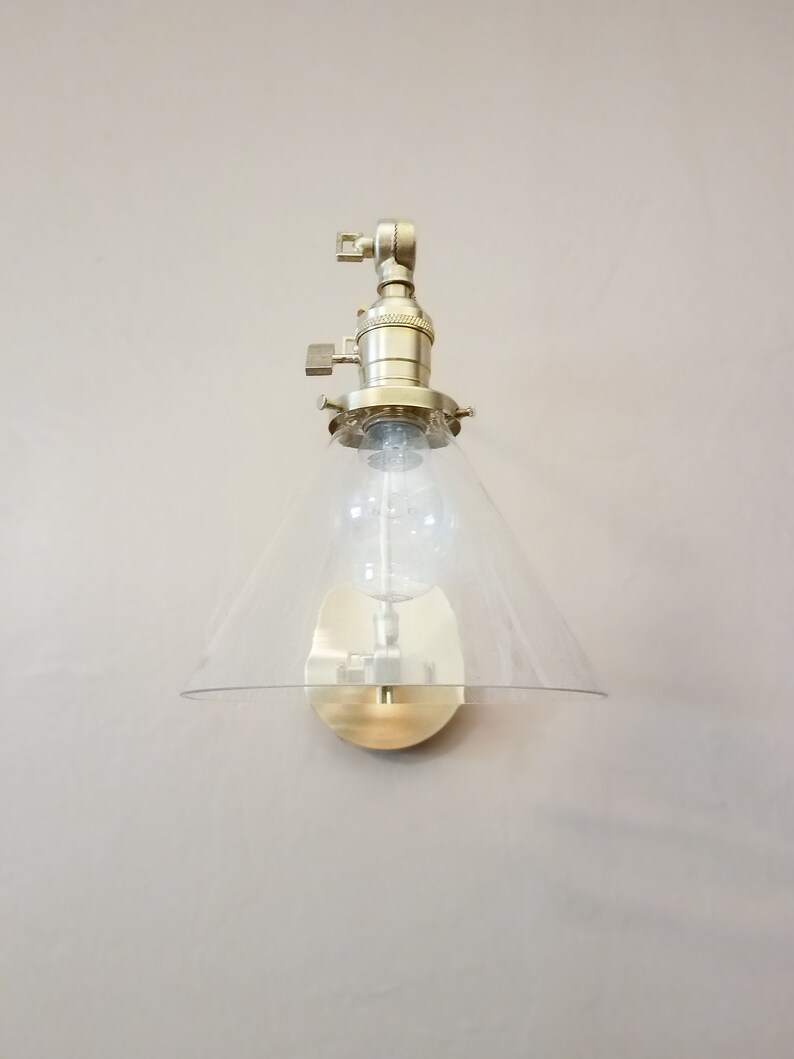 May include: A gold-toned wall sconce with a clear glass cone shade. The sconce has a simple design and is perfect for adding a touch of modern style to any room.