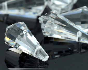 May include: A group of clear crystal teardrop-shaped pendants with faceted edges. The pendants are scattered on a black surface.