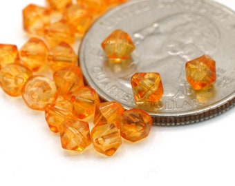 Puede incluir: Un montón de pequeñas cuentas de vidrio facetadas de color naranja junto a una moneda de veinticinco centavos de dólar estadounidense. Las cuentas son aproximadamente del tamaño de un grano de arroz.