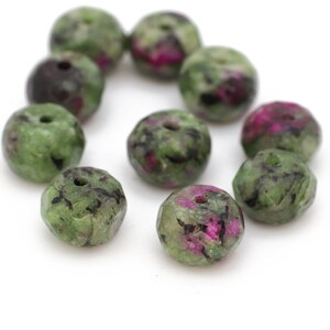 Può includere: Una collezione di perline di pietre preziose verdi e rosa con macchie nere. Le perline sono sfaccettate e hanno un foro praticato al centro.