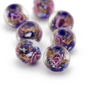 May include: A collection of eight round glass beads with a mix of purple, pink, gold, and white colors. The beads have a translucent appearance and feature swirls of color and gold flecks.
