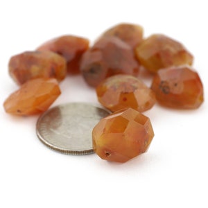 May include: A group of eight faceted carnelian beads, some of which are orange and some of which are brown, are arranged on a white surface. A US quarter is included for scale.