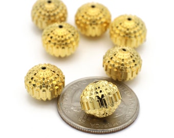 May include: Several gold-colored, textured beads with a detailed, ridged design. The beads are spherical with a small hole at the top. One bead rests on a quarter coin for size comparison. The beads are likely for jewelry making.