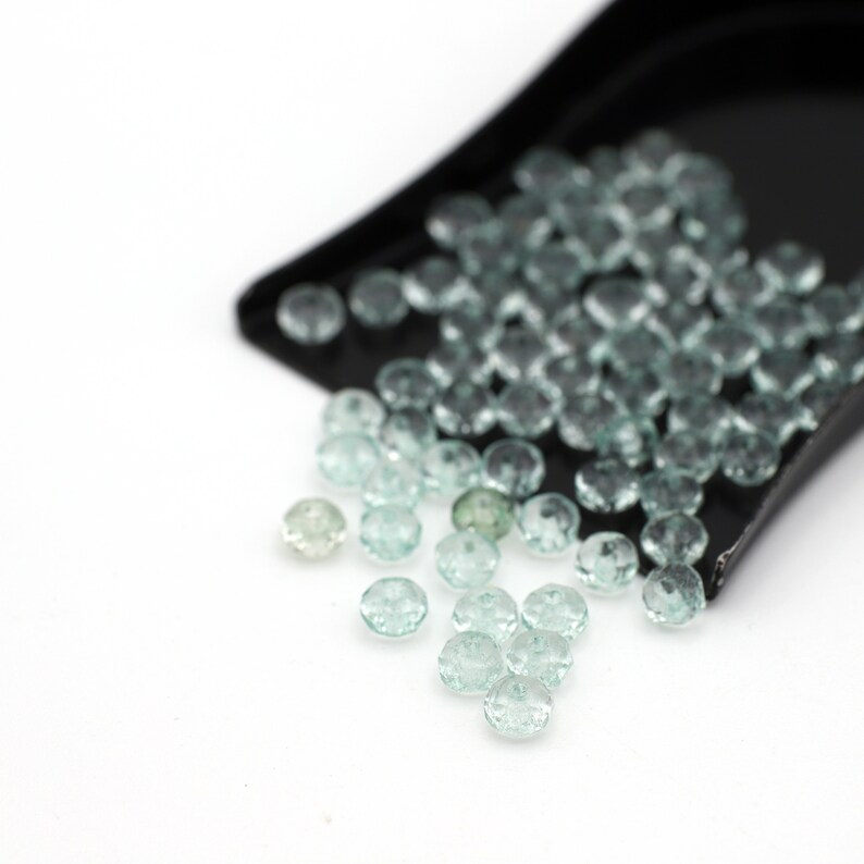 Puede incluir: Una pala llena de piedras preciosas facetadas de color azul claro, con algunas que se derraman sobre una superficie blanca.