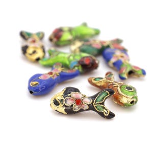 May include: A collection of colourful enamel fish charms with gold accents. The fish are in various shades of blue, green, red, and orange. The charms are ideal for jewellery making or adding a touch of whimsy to any project.