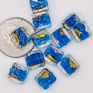 May include: A group of ten square glass beads with a blue and white marbled effect and gold flecks. The beads are approximately the size of a UK 20 pence coin.