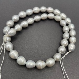 May include: A strand of grey pearl beads, strung on white thread. The pearls are oval shaped and have a smooth, lustrous finish.