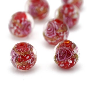 May include: A collection of red glass beads with white and pink swirls and gold flecks. The beads are round and have a glossy finish.