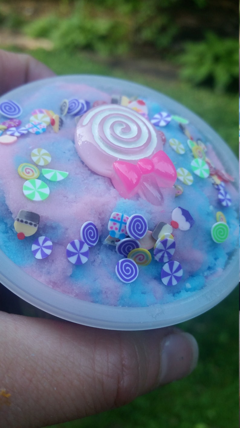 Peut inclure: Un r&eacute;cipient en plastique transparent rempli de slime bleu et rose avec une vari&eacute;t&eacute; de paillettes color&eacute;es et une sucette rose et blanche sur le dessus.
