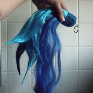 Pode incluir: Uma extensão de cabelo azul e turquesa com um clipe preto. A extensão de cabelo é longa e fluida.