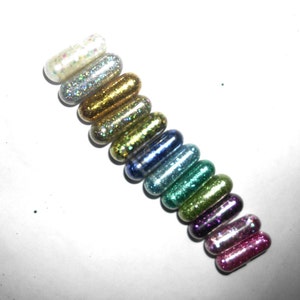 May include: A row of 14 small, colorful, glitter-filled capsules. The capsules are arranged in a rainbow pattern, starting with silver and ending with pink.