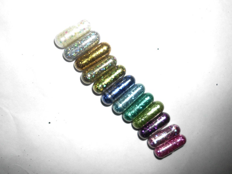 May include: A row of 14 small, colorful, glitter-filled capsules. The capsules are arranged in a rainbow pattern, starting with silver and ending with pink.