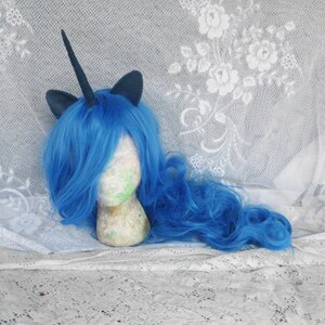 May include: A blue wig with a black unicorn horn and ears. The wig is on a white mannequin head.