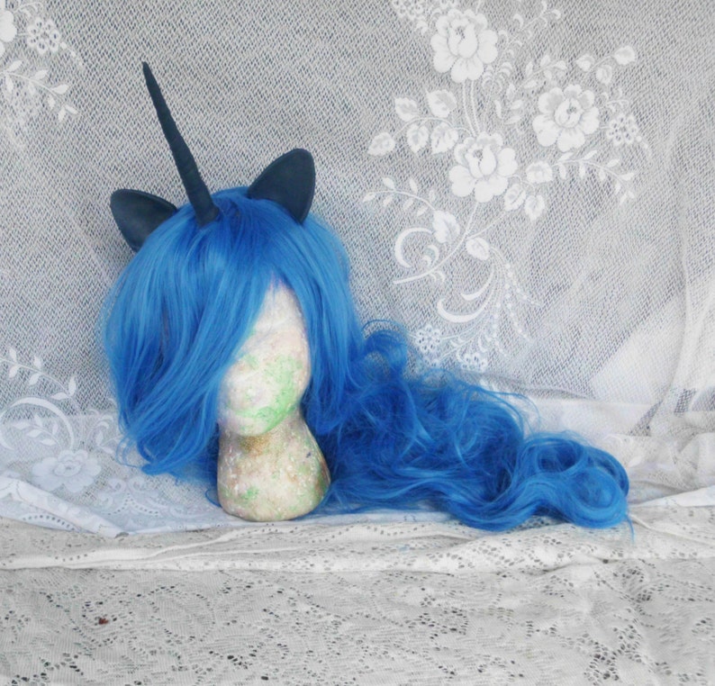 May include: A blue wig with a black unicorn horn and ears. The wig is on a white mannequin head.