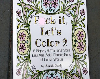 May include: The cover of an adult coloring book titled "Fck it, Let's Color 2: A Bigger, Better, and More Bad Ass Adult Coloring Book of Curse Words" by Sarah Ganly. The cover features a floral design with pink and yellow flowers.