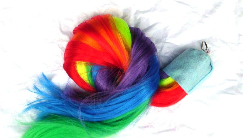 May include: A rainbow-colored ponytail hair extension with a light blue felt pouch attached to a silver key ring.