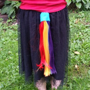 May include: A rainbow-colored ponytail extension attached to a black skirt with a blue band around the base.