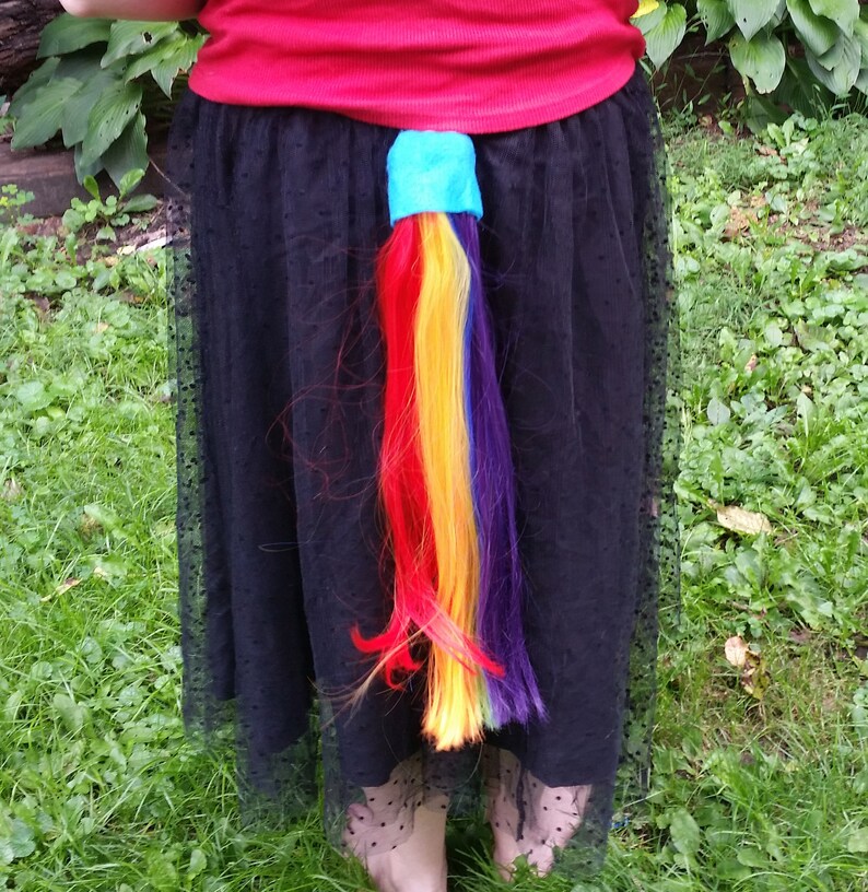 May include: A rainbow-colored ponytail extension attached to a black skirt with a blue band around the base.