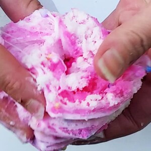 Puede incluir: Slime esponjoso rosa y blanco con chispas de colores. El slime est&aacute; siendo sostenido en dos manos.
