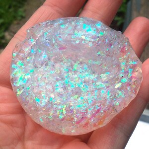 Puede incluir: Un slime transparente e iridiscente con una textura brillante. El slime es de color azul claro con toques de rosa y verde.