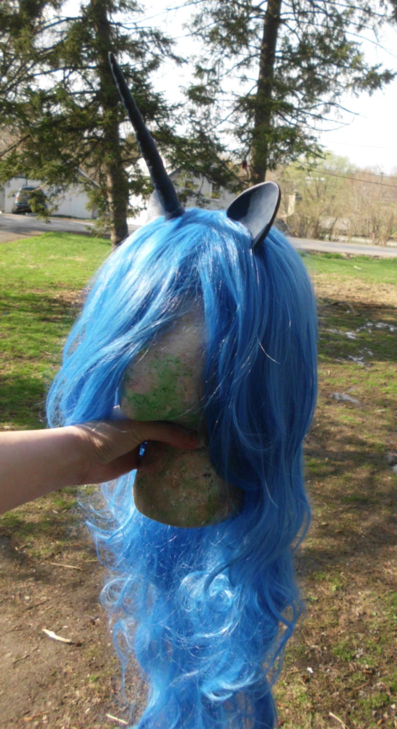 May include: A blue wig with a black unicorn horn and ears. The wig is on a mannequin head.