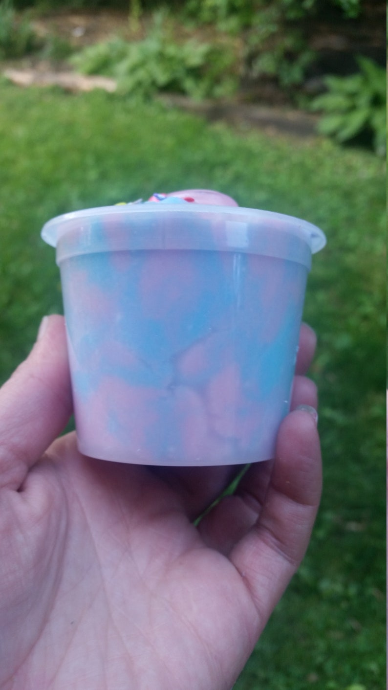 Peut inclure: Un r&eacute;cipient en plastique transparent rempli de slime rose et bleu en spirale. Le slime a un aspect marbr&eacute;.