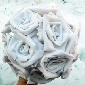 May include: A bouquet of white fabric roses, crafted from white cotton fabric, arranged in a circular shape.