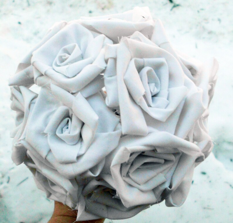May include: A bouquet of white fabric roses, crafted from white cotton fabric, arranged in a circular shape.